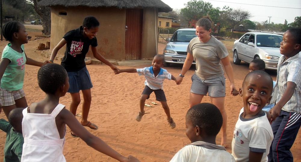 Children in Botswana and Pitzer student hold hands in a circle.